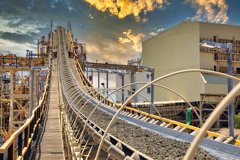 Galería de correa transportadora elevada hacia una planta de procesamiento al atardecer