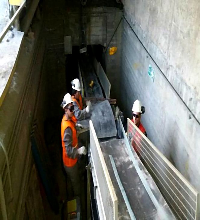 Técnicos trabajando sobre una correa transportadora dentro de un túnel de planta